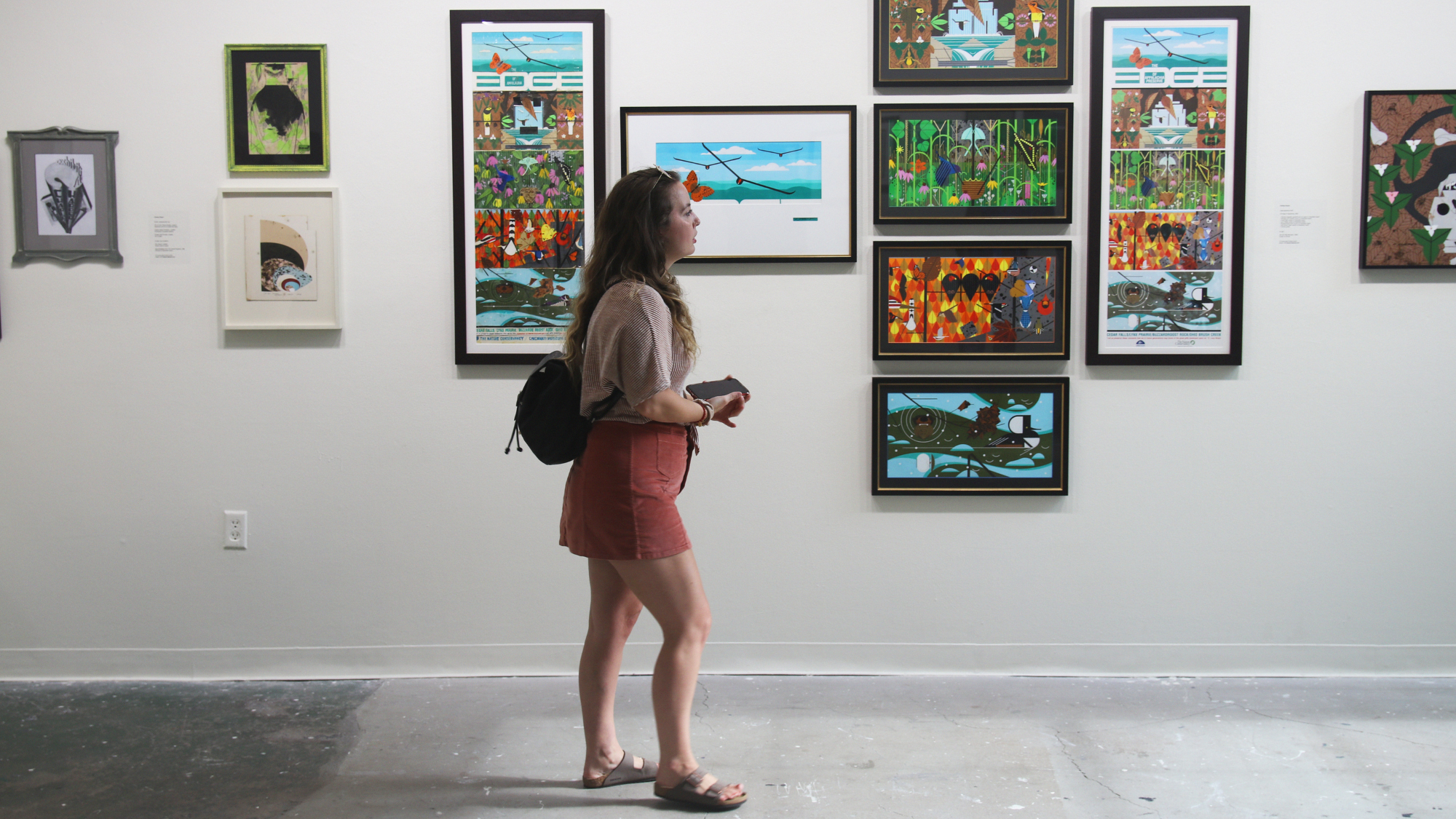 Young white woman walks through gallery space with colorful print media framed on a white wall