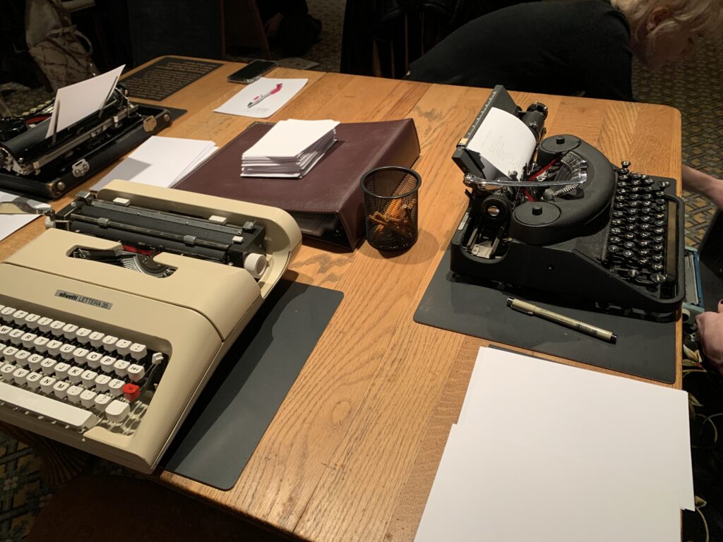 three typewriters on a table with pens and paper