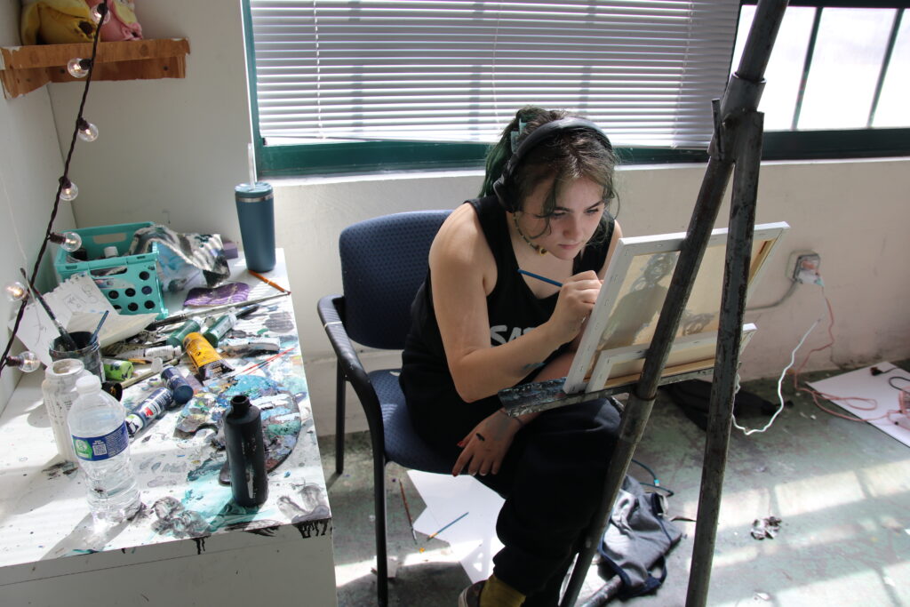 Teen Future BFA portfolio prep student painting in studio with a messy paint table and easel.