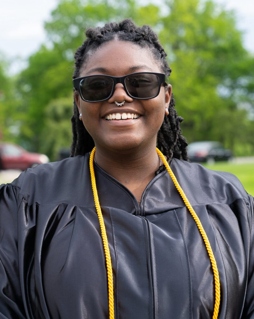 photo of a young woman in graduation gown and yellow tassels smiling.