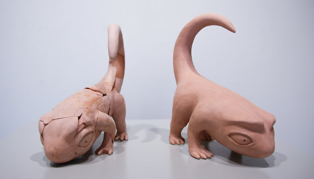 Two statues of a stylized lizard; one pristine, one cracked.