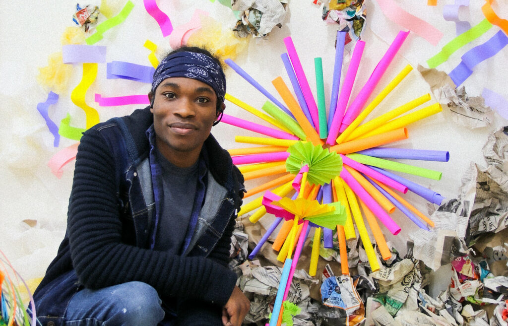 La'De Richardson standing in front of a vibrant sculpture made out of paper and other soft materials.