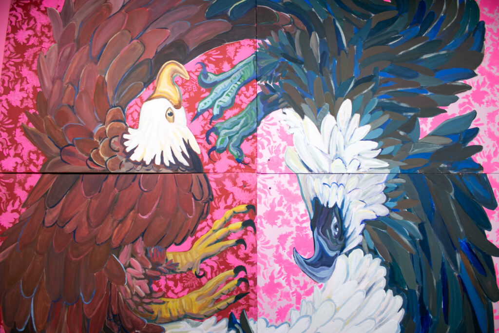 A painting of two eagles, one in negative and one in normal colors, atop a flowery pink background. The painting is made of four smaller pieces.