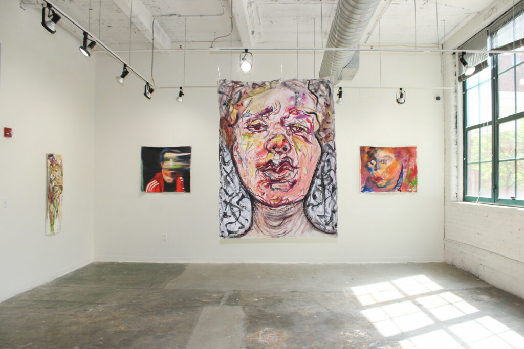 A stylized painting of a face in the center of a large, well lit gallery space.