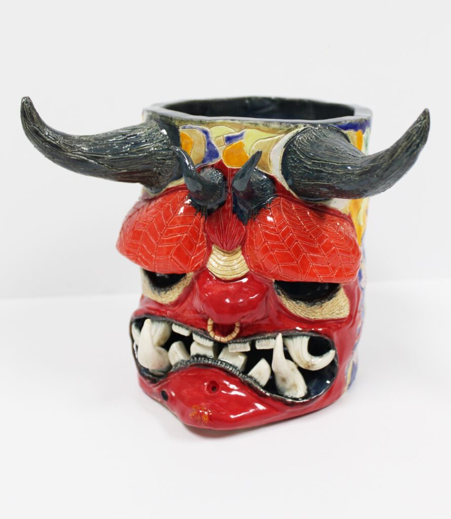 A ceramic vessel depicting a horned figure with a large brow, red skin, and gnarled tusklike teeth