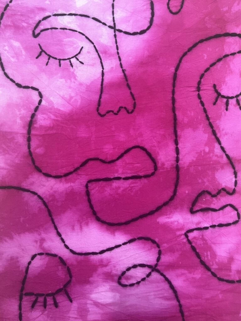 A mixed media depiction of abstract faces sewn into pink fabric