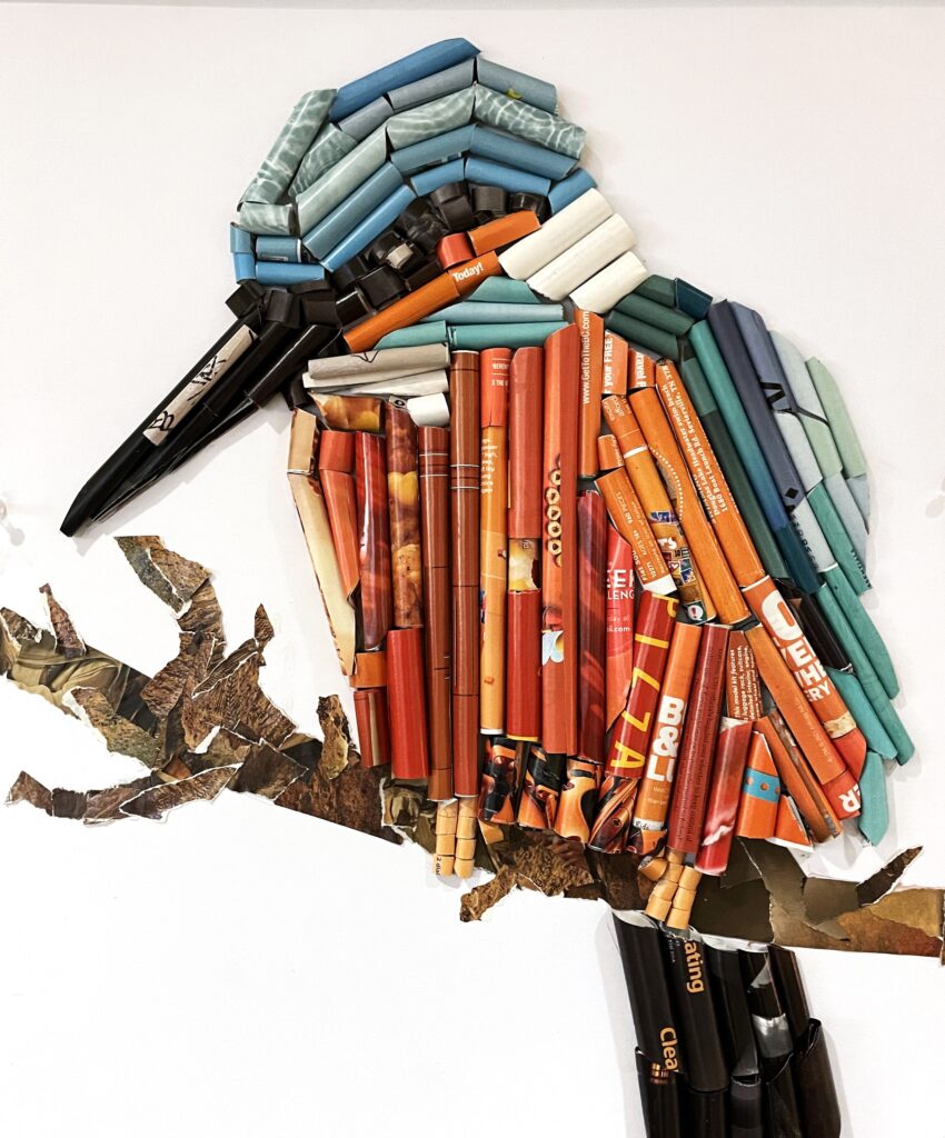 A mixed-media collage depicting a large-beaked bird on a branch. The bird itself is made out of the remnants of crayons, charcoal, and pencils.