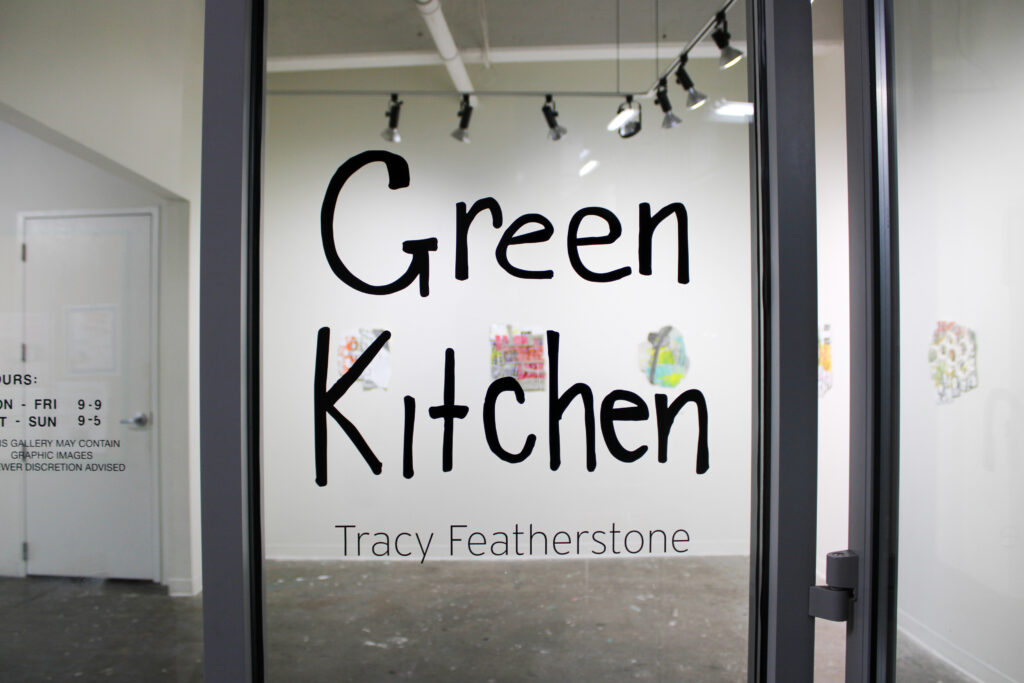 A window into a gallery space; center frame is a decal that says "green kitchen"