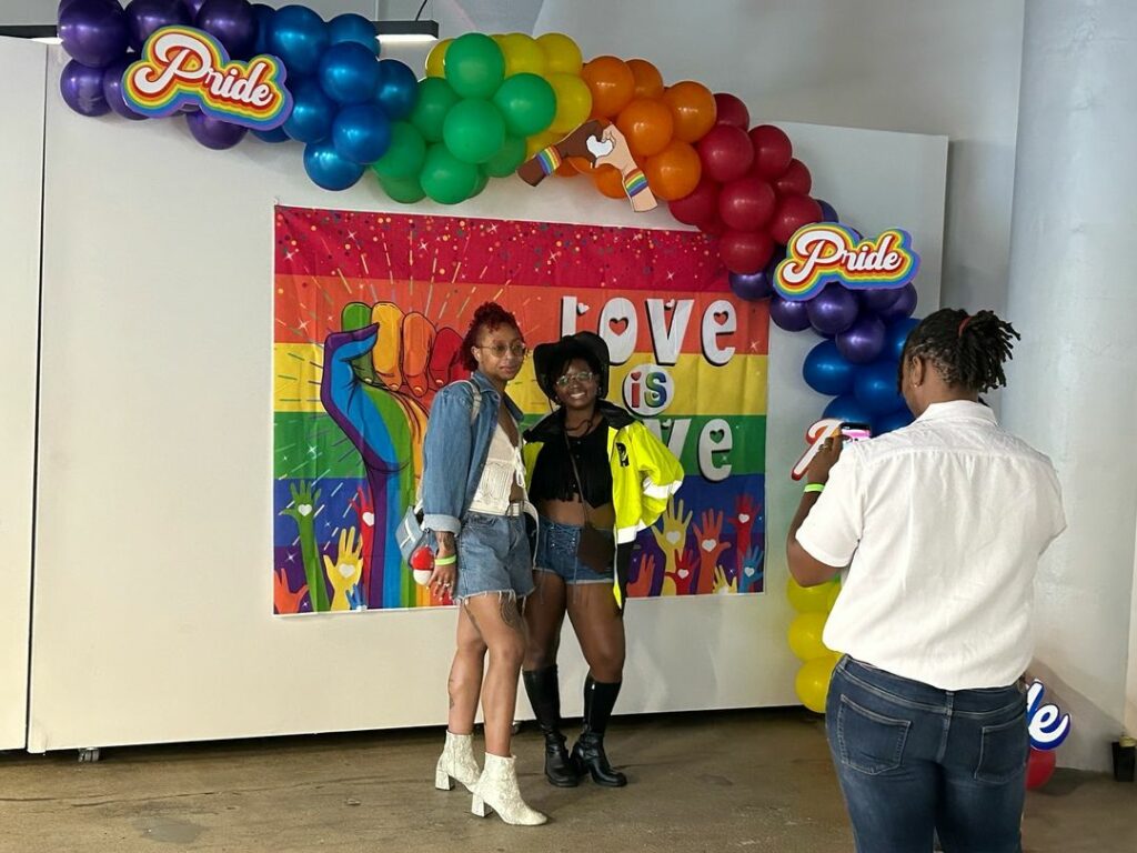 two students having photos taken of them in front of a pride flag