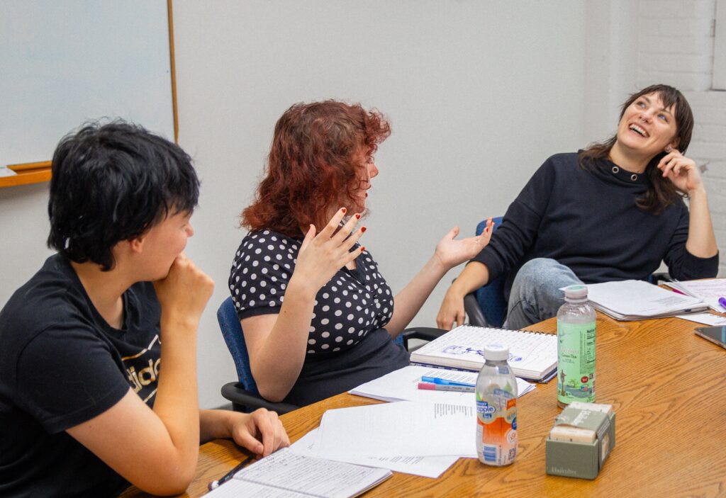 Instructor and two students around a table talking about their writing