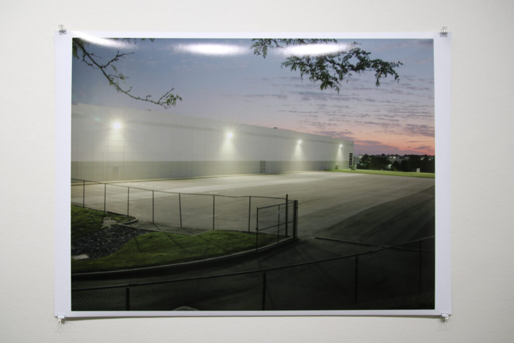 A photo on a white wall with a large photo that shows an industrial facility and parking lot at dawn.